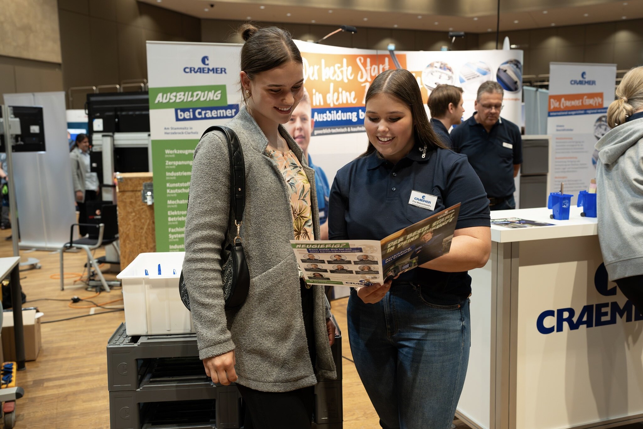 Craemer Auszubildende präsentiert einer Besucherin am Stand einen Flyer