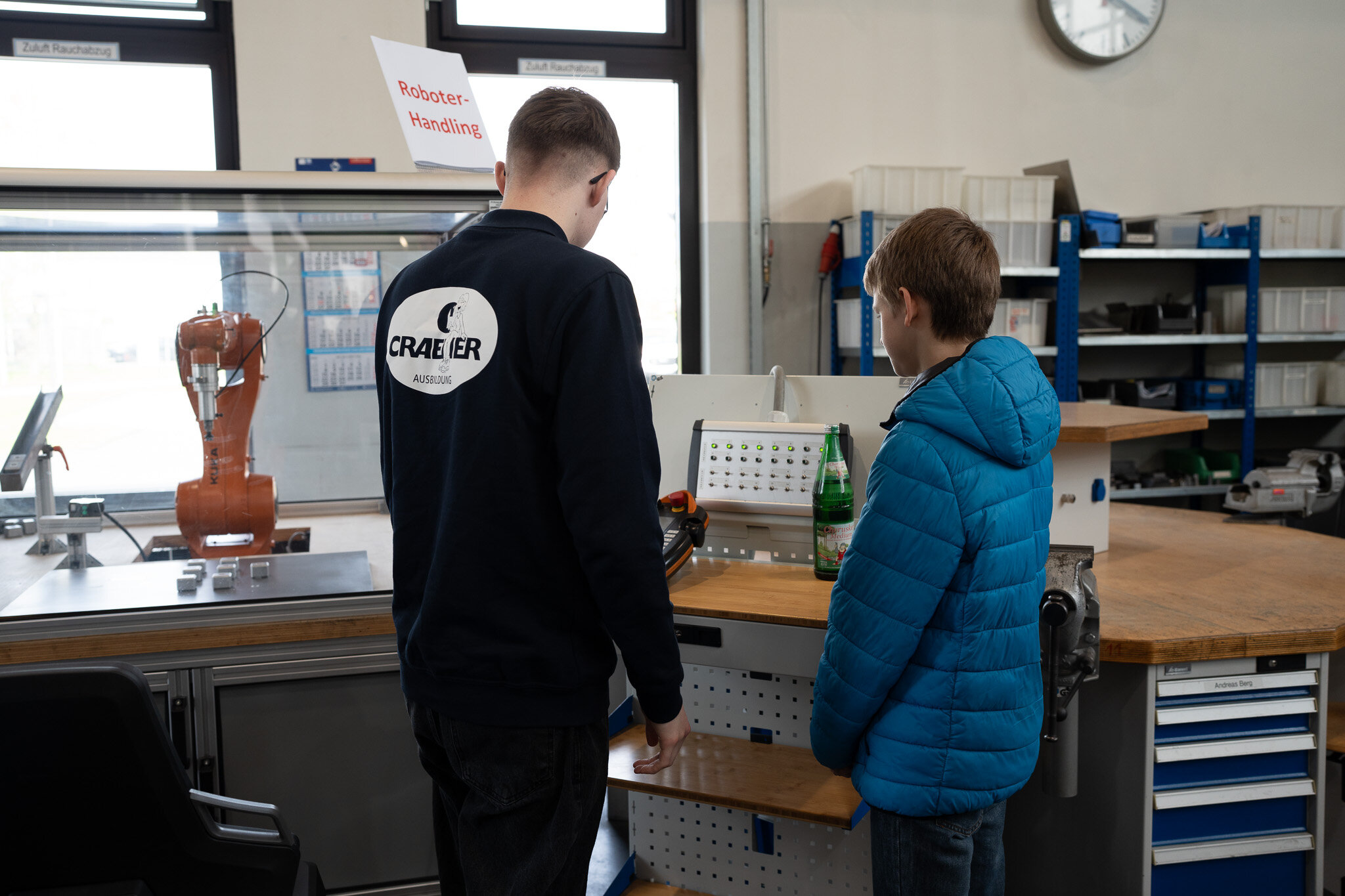 Craemer Auszubildender zeigt einem jungen Schüler etwas am Präsentationstisch Roboter Handling